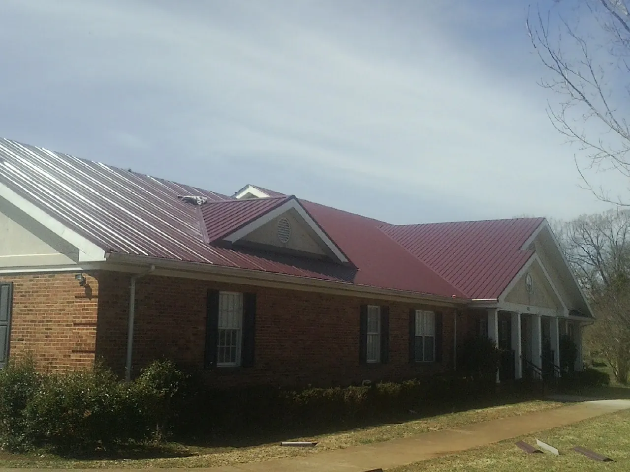 Red metal roof with gabled entries on a long brick building, from a Hail Damage Roof Repair job in Letohatchee
