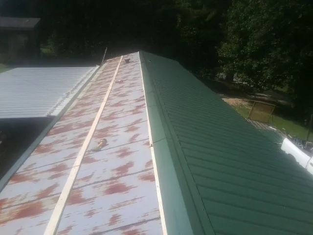 Old rusted panels beside newly installed green metal roofing — Wind Damage Roof Repair by Roofing Brothers in Letohatchee