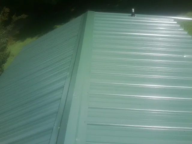 New green metal panels meeting at the ridge of a roof — Flat Roof Repair work by our crew in Letohatchee