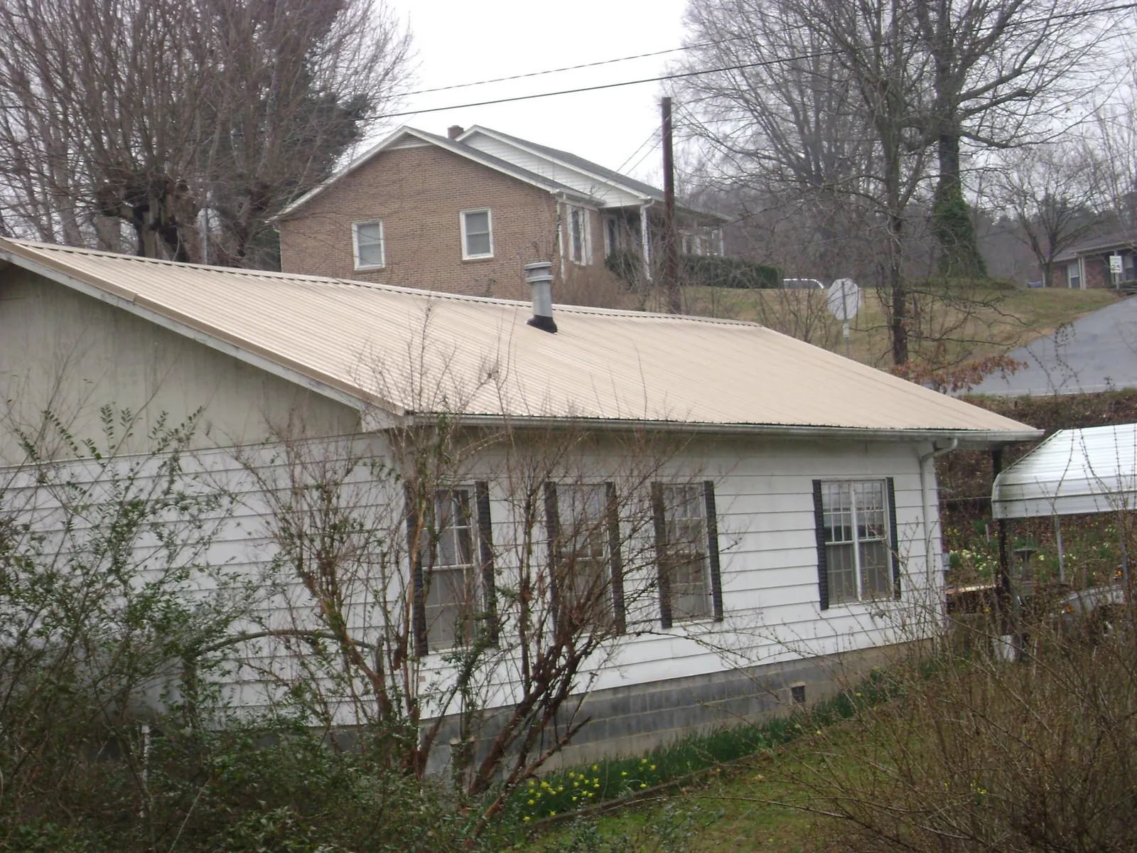 Tan metal roof on a white sided house set into a hillside — Commercial Roofing by Roofing Brothers in Letohatchee