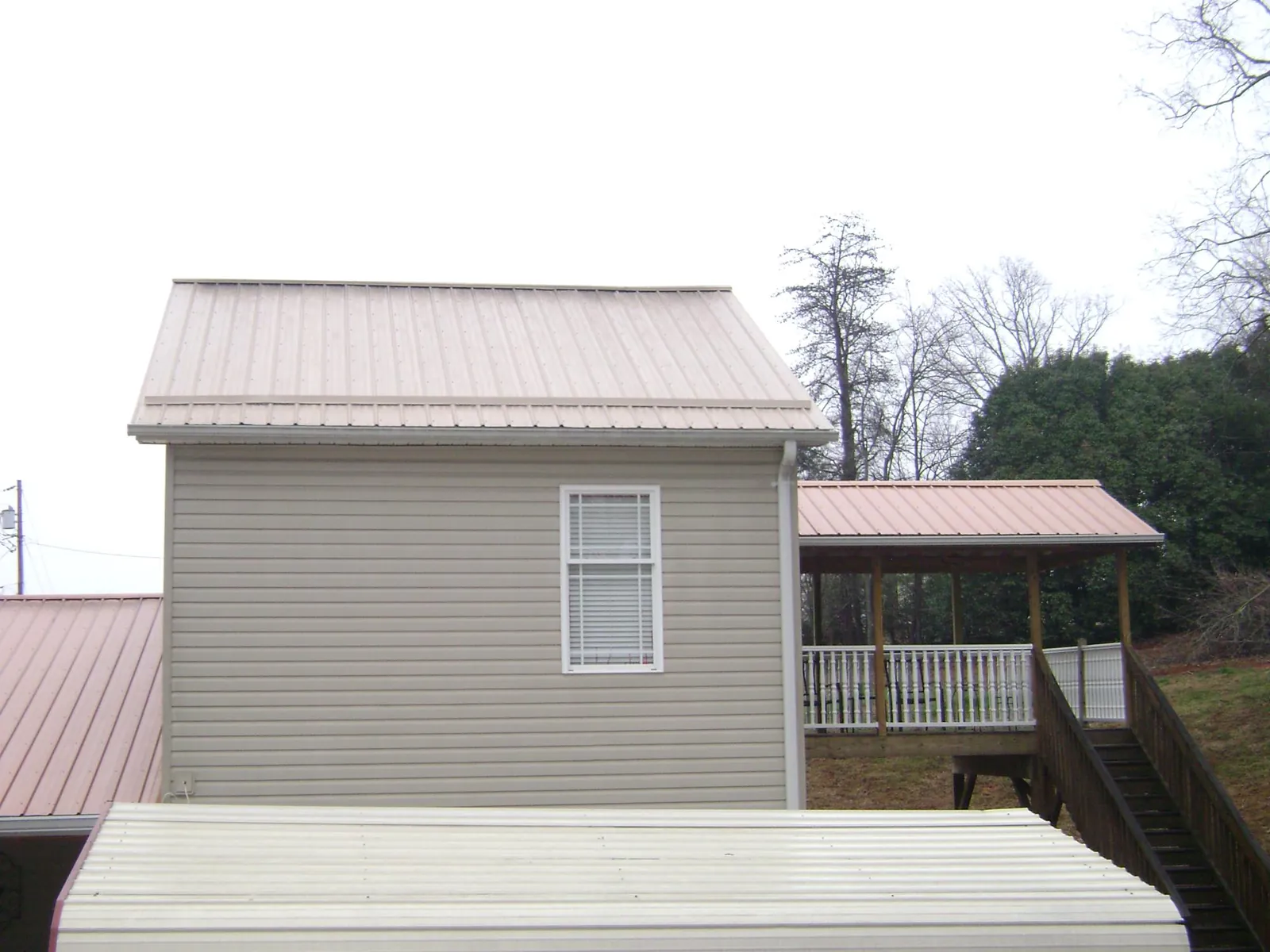 Tan metal roofs on a two story addition and attached porch, from a Roof Replacement job in Letohatchee
